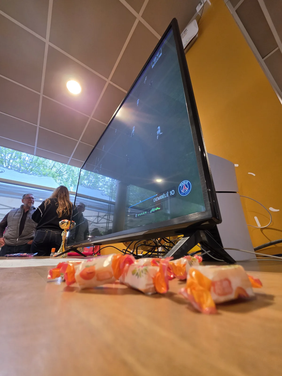 Bonbons disposés au premier plan devant l'écran du jeu FIFA, ambiance lumineuse et conviviale du stand